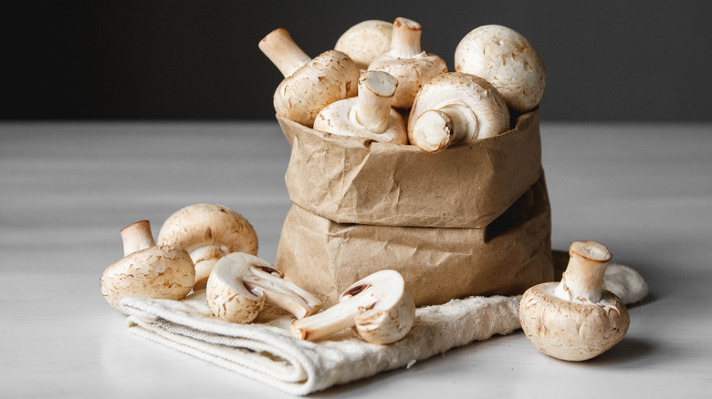 Button mushrooms in brown paper bag on kitchen towel