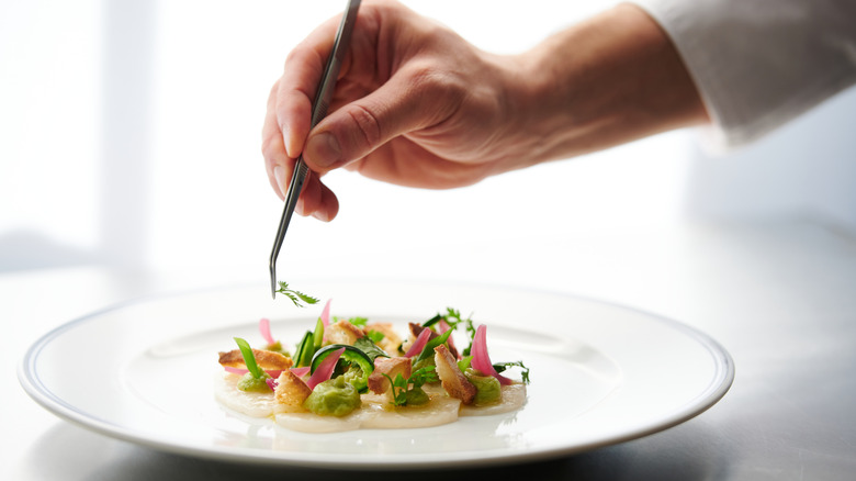 chef using tweezers to garnish an elegant plate