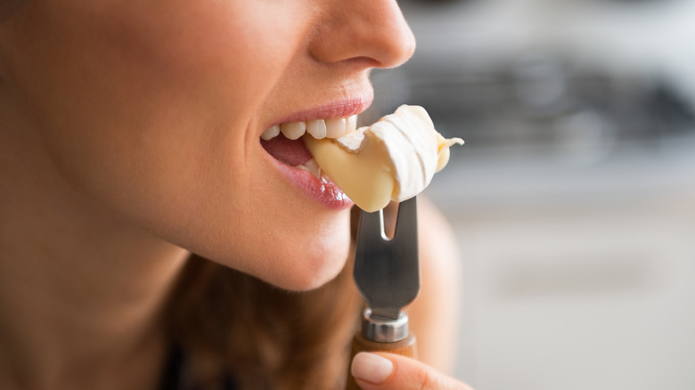 Woman takes a bite from a wedge of brie cheese