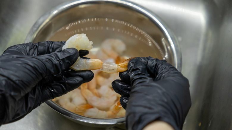 Gloved hands prepare shrimp in a sink