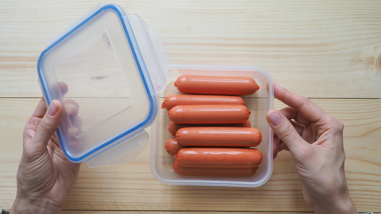 Hands holding a plastic container with hot dogs and a lid