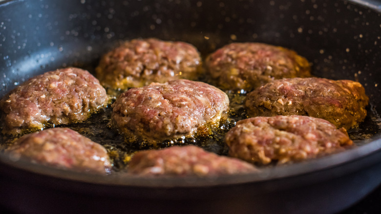 Hamburgers being cooked in a pan with oil