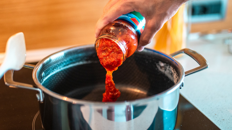 Pouring jarred tomato sauce into a stockpot.