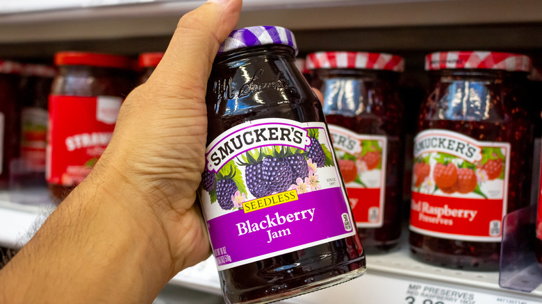 Man's hand picking up jar of Smucker's Blackberry Jam from grocery shelf