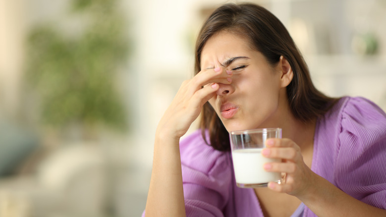 A woman holding her nose with one hand while lifting a glass of milk.