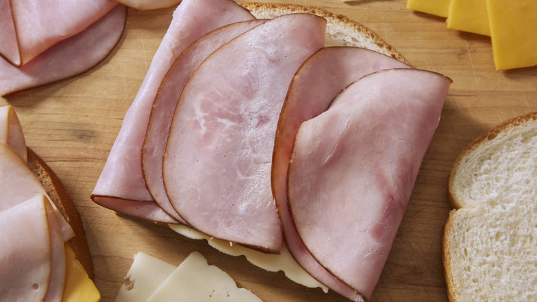 Sandwich bread with slices of ham and cheeses in the background.