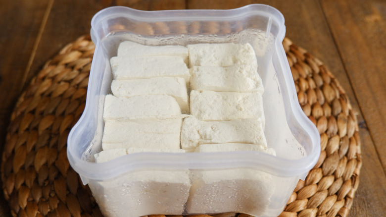 Tofu slices submerged in fresh water in a plastic container