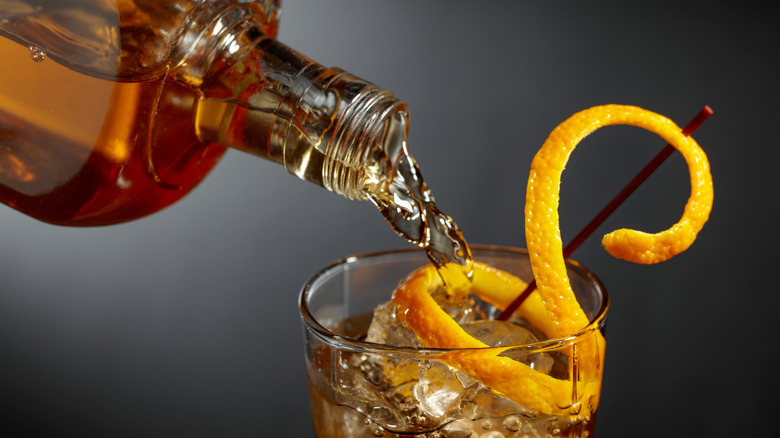 Bottle of bourbon being poured in a glass with orange twist