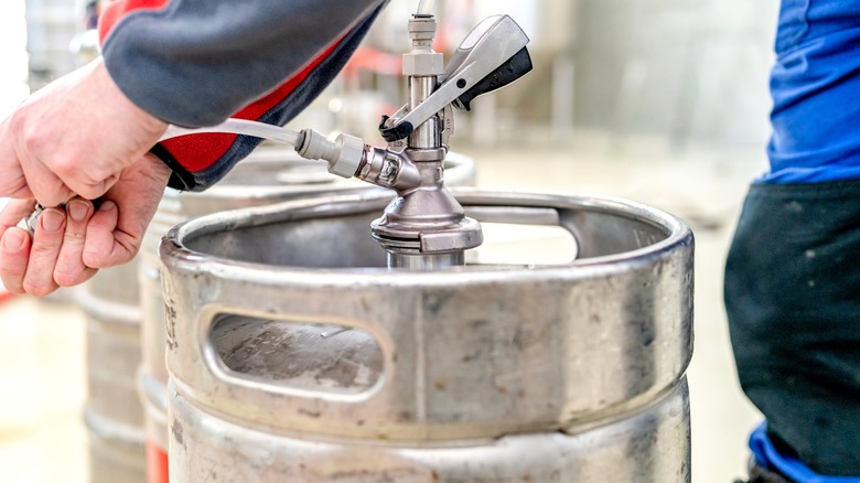 A person hooking up a beer keg to a tap.