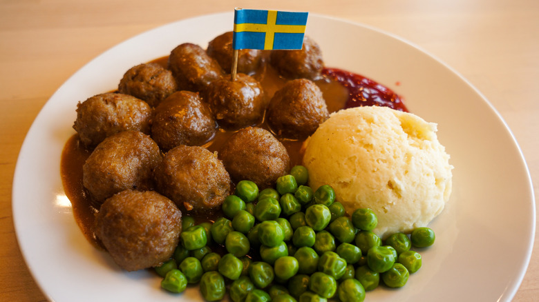 Swedish meatballs on white plate with peas, mashed potatoes, and small Swedish flag