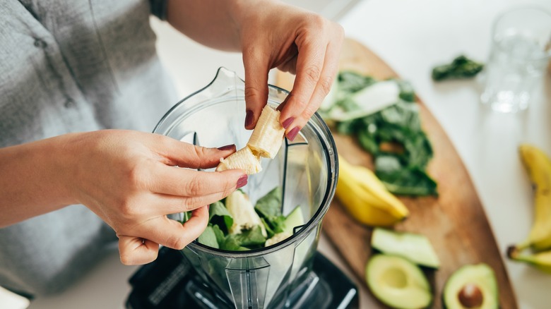 woman putting a banana into a blender to make a green smoothie