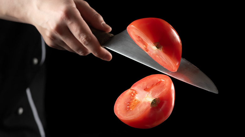 hand holding a knife as it cuts through a tomato in midair 