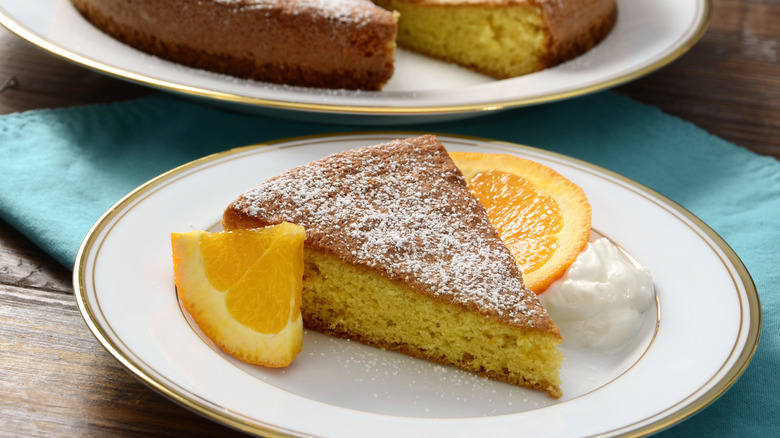 Slice of cake topped with powdered sugar with orange slices on the side