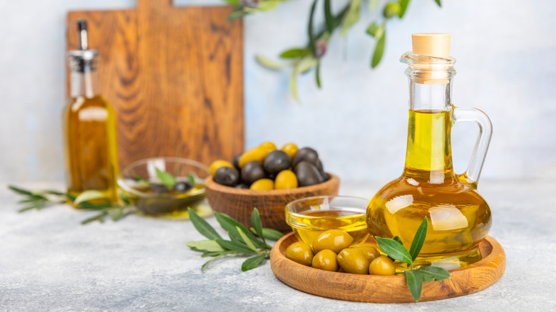 Decanter of olive oil on a wooden plate with green olives