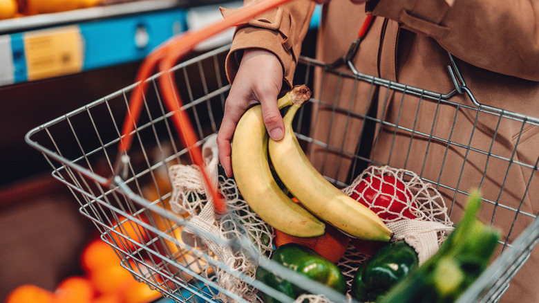 Adding a few bananas to fresh produce in a grocery basket