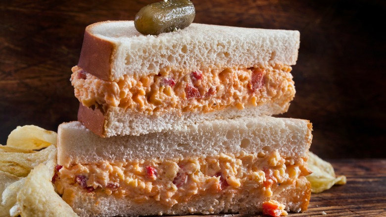 Pimento cheese sandwich on wood table with chips on side