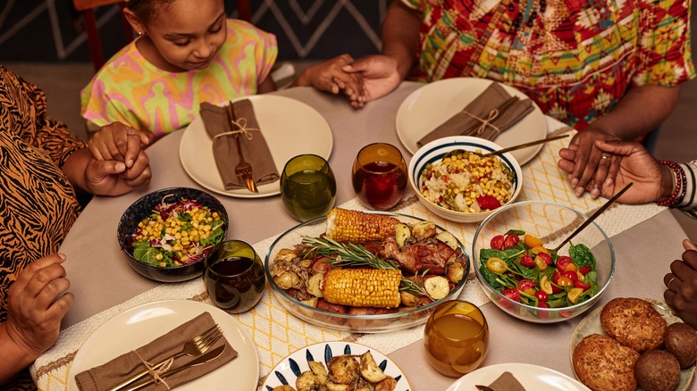 A little girl holding hands of others while gathered around the dinner table.