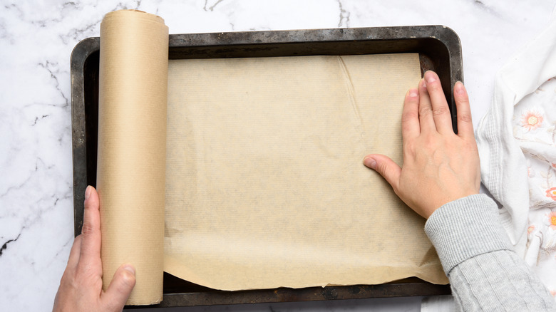 Person rolling parchment paper onto a baking sheet