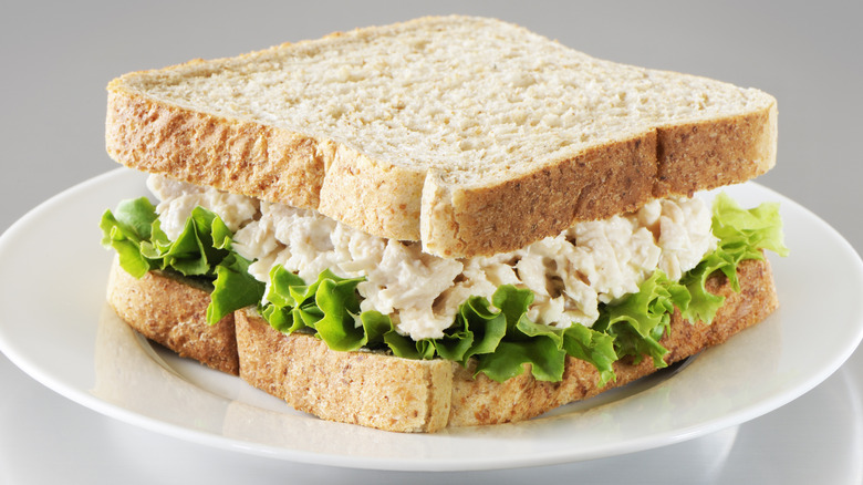 Tuna sandwich on wheat bread with lettuce on a white plate.