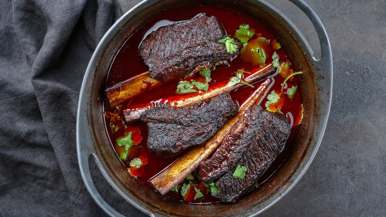 Short ribs braising in red liquid and herbs