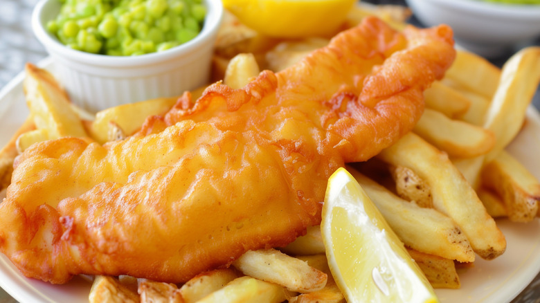 Plate of fish and chips with a side of mushy peas and a lemon wedge.