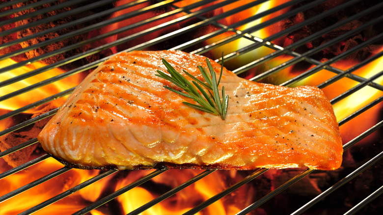 Salmon grilling over open flames with sprig of rosemary