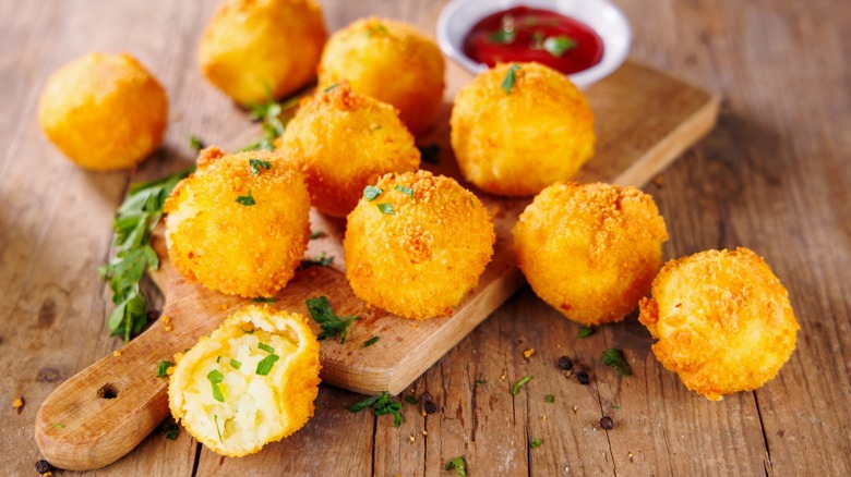 Arancini on wood board with one opened showing cheesy filling