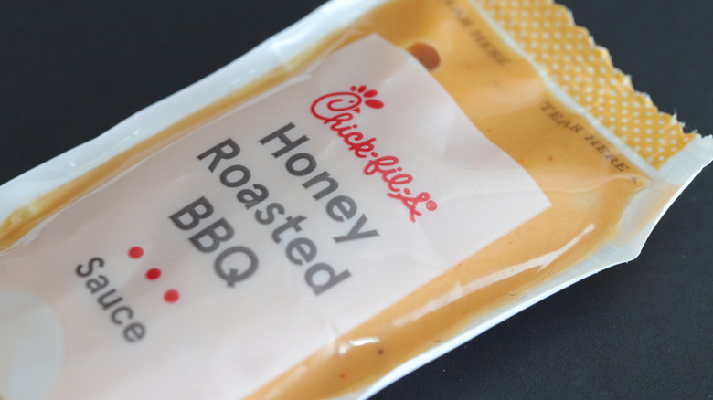 A packet of orange-colored Chick-fil-A Honey Roasted BBQ sauce is isolated against a black background