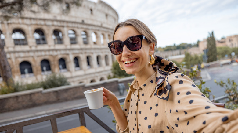 Woman with cup of espresso in front of the Colosseum. 