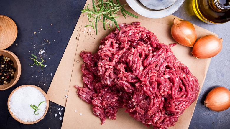 Ground meat on brown paper alongside seasonings, dark tabletop.