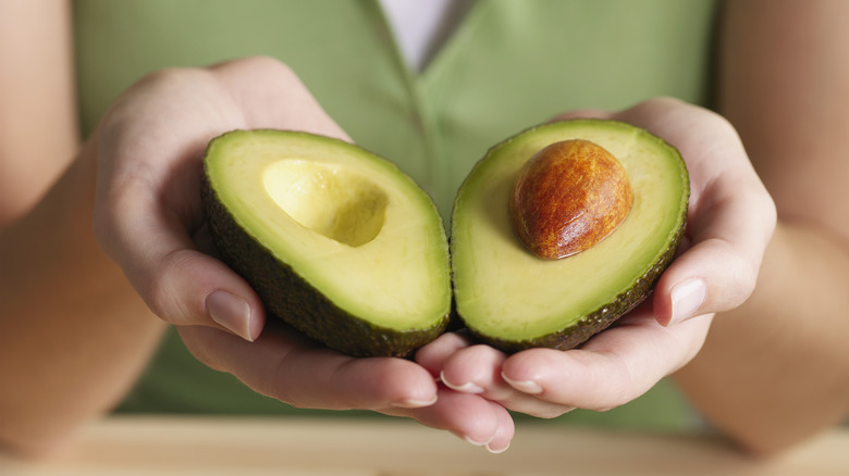 woman holding an avocado cut in half