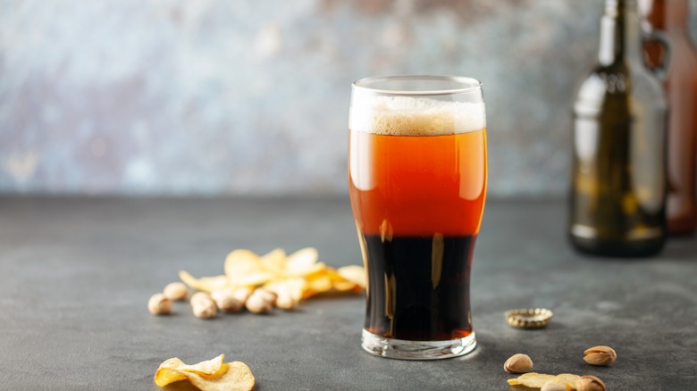 Black and tan beer on a table with peanuts and potato chips