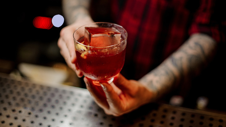 Hands serve a Vieux Carre cocktail over a bar