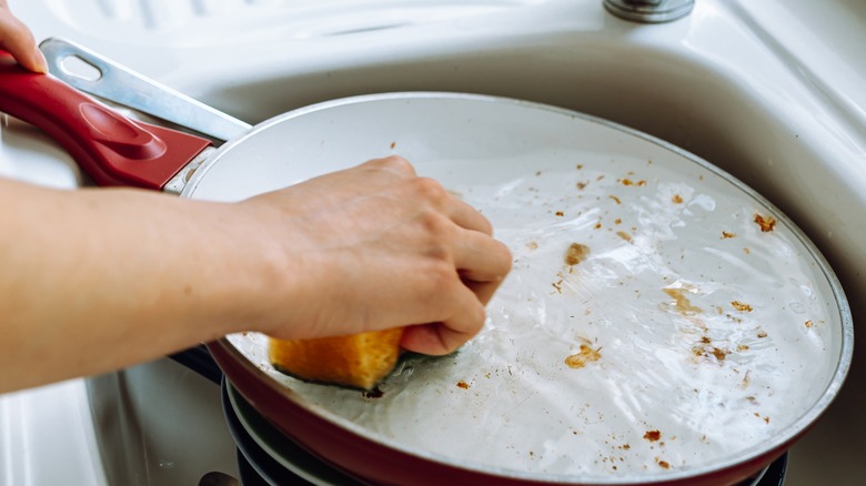 Person scrubbing dirty ceramic pan in sink