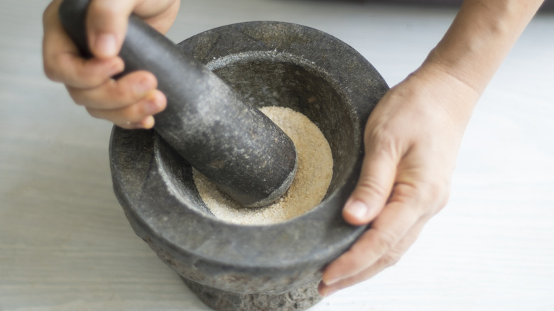 Hands use a mortar and pestle to grind rice