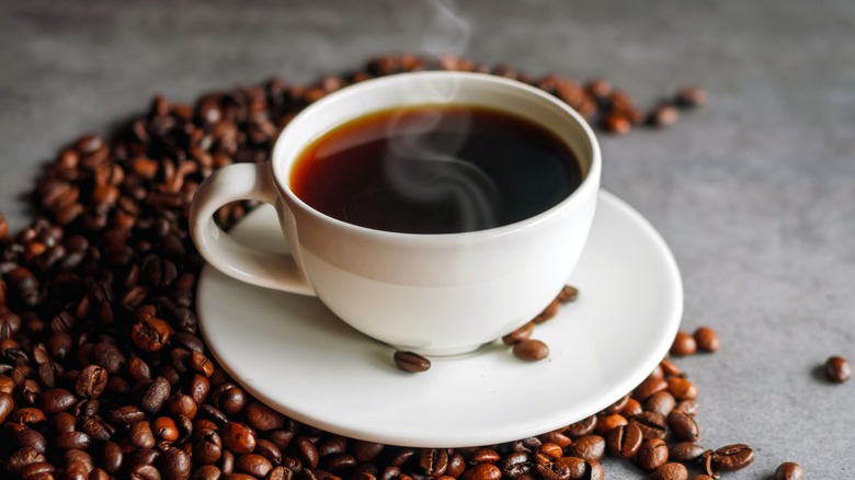 Steaming cup of coffee on top of whole coffee beans