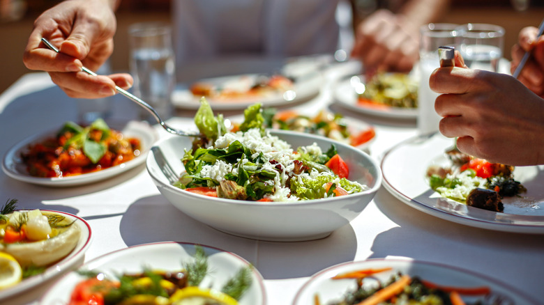 White bowl of vibrant salad between other plates of food being eaten.