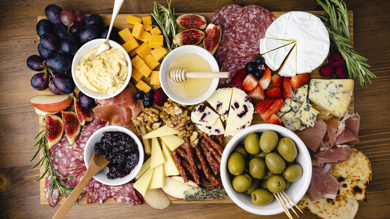 Charcuterie board with a variety of fruits, meats, cheeses, spreads, and herbs