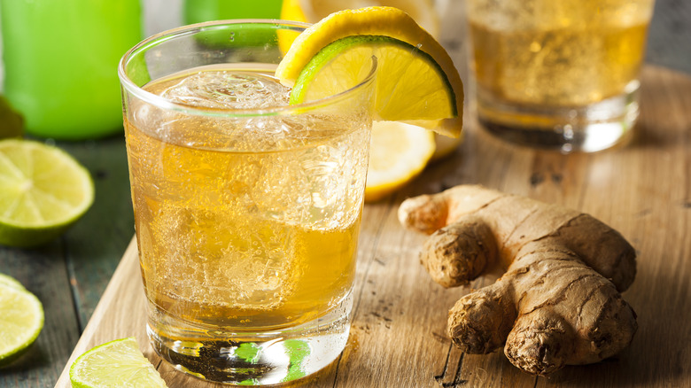 Glass of ginger ale with bottle, ginger and lemons
