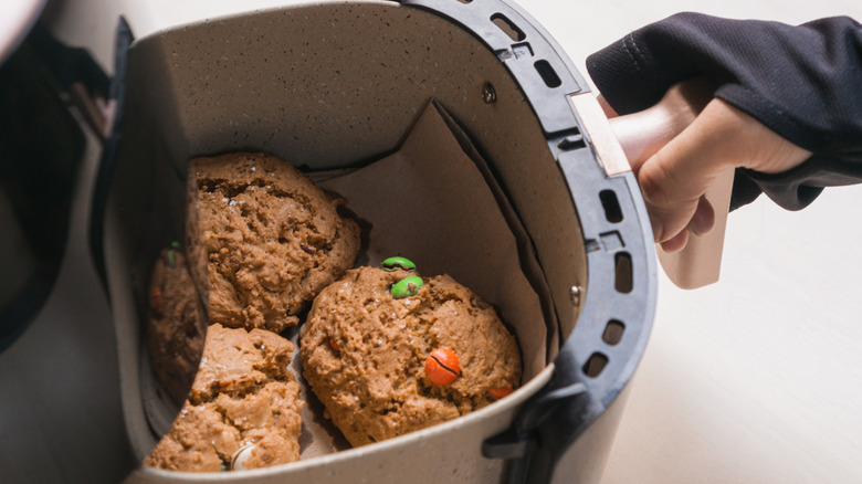 Hand pulling out air fryer basket containing cookies.