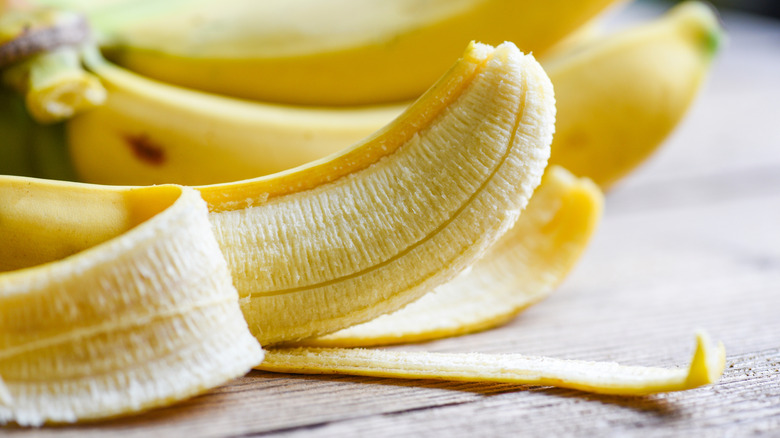 A closeup of a peeled banana with bananas behind it.