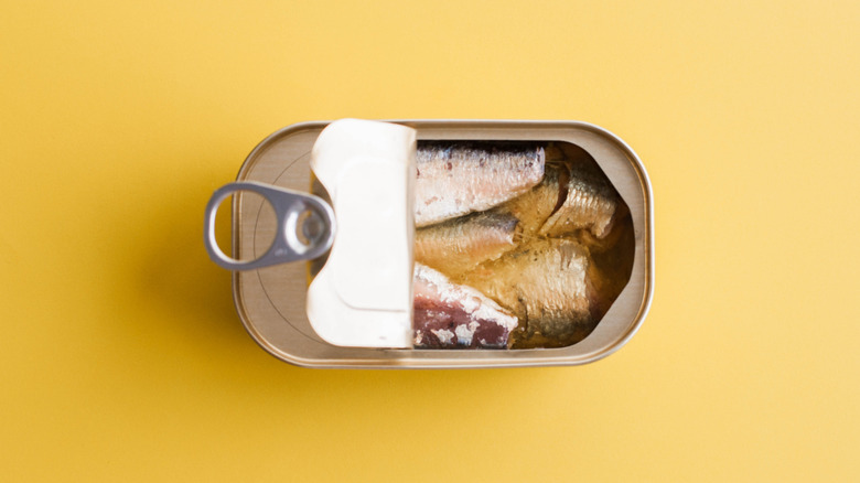 Overhead view of canned sardines on yellow background, top partially open.