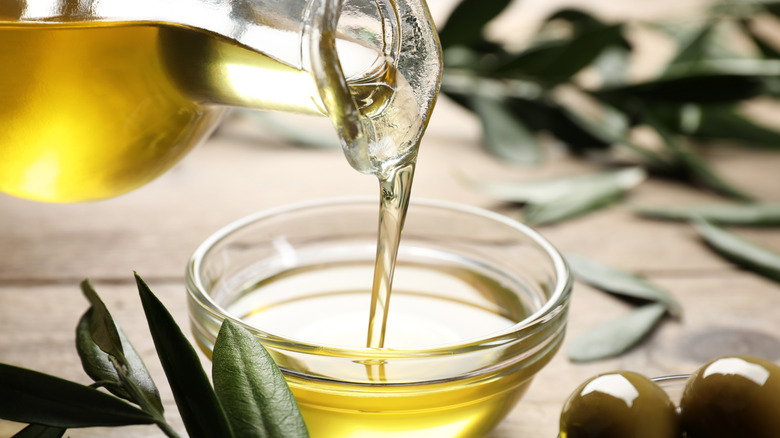 Jar of olive oil pouring in a small dish.