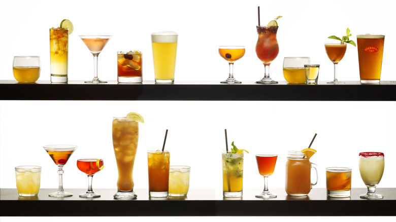 Many different cocktails brightly backlit on white background and black shelves.