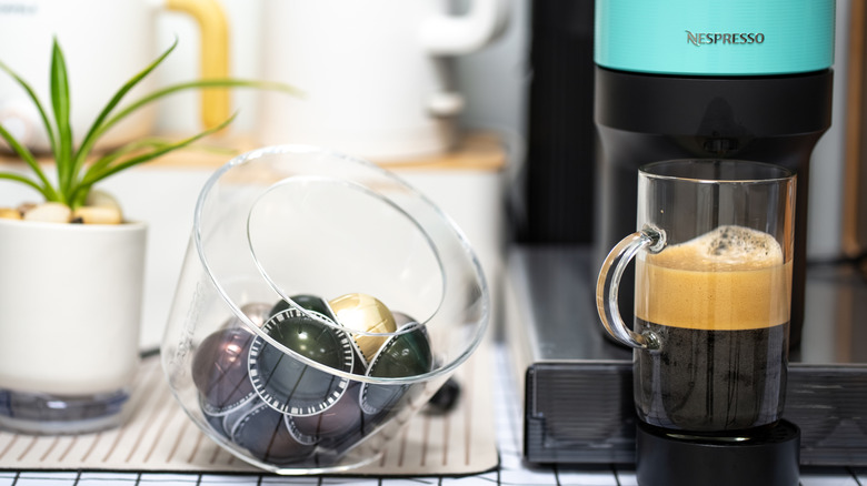 Nespresso coffee machine with a coffee brewing next to coffee pods and a plant