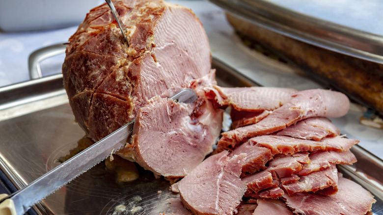 Knife slicing thin slices of honey ham on metal tray