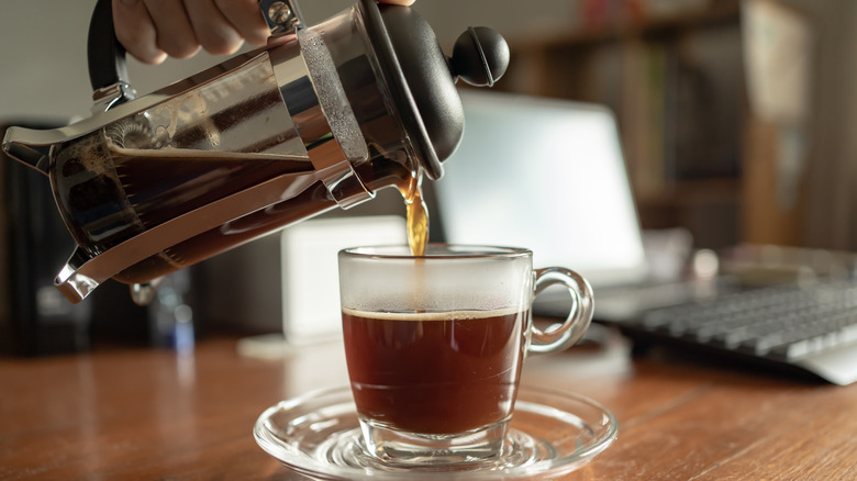 Coffee pouring from a french press into a glass mug