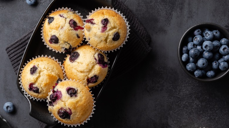 Blueberry muffins in tray with blueberries nearby