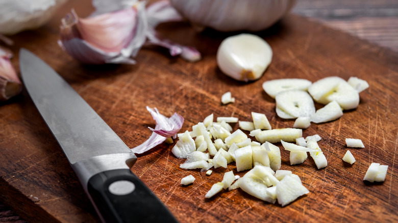 knife resting next to chopped garlic on cutting board