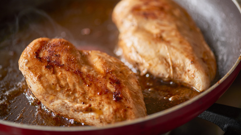 two pieces of chicken cooking in a pan